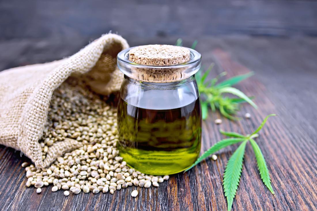 hemp oil in glass bottle next to hemp seeds and leaves on wooden table